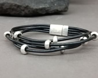 May include: A black leather bracelet with a silver magnetic clasp and silver beads.