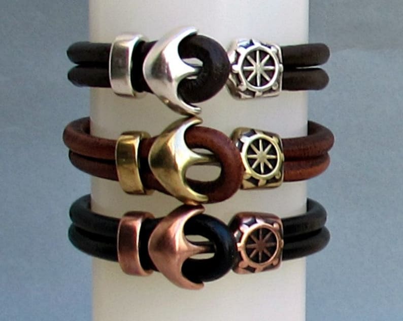 May include: Three leather bracelets with anchor and compass charms. The bracelets are brown, black, and brown with silver, brass, and copper accents.