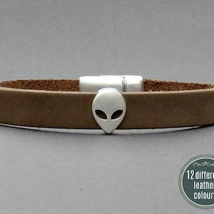 Peut inclure: Un bracelet en cuir marron avec un charme tête d'alien argenté.