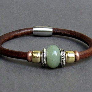 Könnte beinhalten: Ein braunes Lederarmband mit einem grünen Steinperlen und silbernen und goldenen Akzenten.