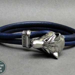 May include: A blue leather bracelet with a silver wolf head clasp. The bracelet is double-layered and has a decorative silver bead detail.