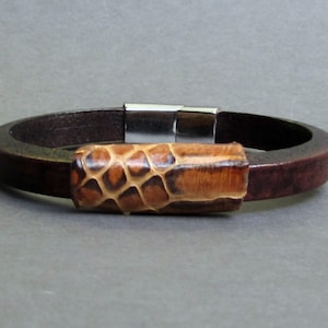 Peut inclure: Un bracelet en cuir marron avec un fermoir magnétique et un accent en cuir à motif marron et beige.