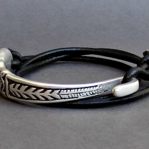 May include: A silver bracelet with a black leather strap. The silver band has a decorative pattern of leaves and is curved.
