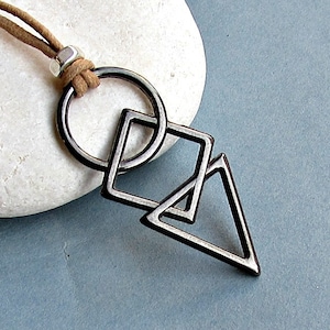 Op de afbeelding: Een ketting van zwart lederen koord met een zilveren metalen hanger met een cirkel, vierkant en driehoek ontwerp.