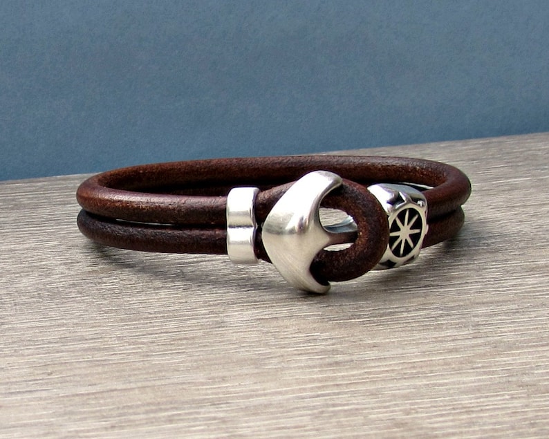 May include: A brown leather bracelet with a silver anchor and compass charm.