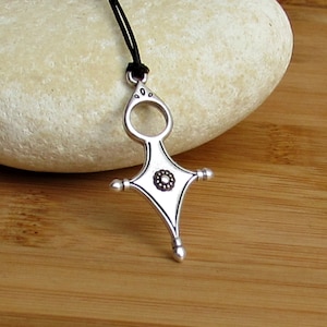 May include: Silver pendant necklace with a star-shaped design and a small circle in the center. The pendant is on a black leather cord.