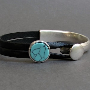 Puede incluir: Un brazalete de cuero negro con una banda de metal plateado y un acento de piedra turquesa.