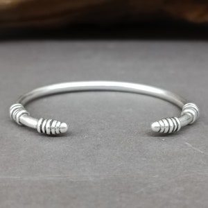 Può includere: Un braccialetto rigido in argento con un design semplice e dettagli testurizzati alle estremità.