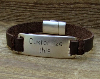 May include: A brown leather bracelet with a silver clasp and a rectangular silver tag that says "Customize this".
