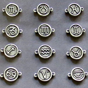May include: Twelve silver charms featuring the astrological signs of the zodiac. Each charm is a circle with a raised design of the zodiac symbol.