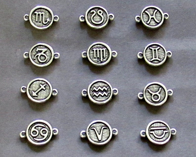 May include: Twelve silver charms featuring the astrological signs of the zodiac. Each charm is a circle with a raised design of the zodiac symbol.