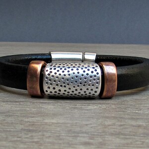 May include: A black leather bracelet with a silver and copper accent. The silver accent has a perforated design.