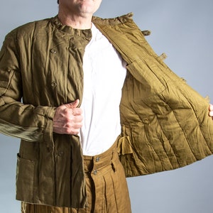 May include: Olive green quilted jacket with a round collar and button closure. The jacket has two front pockets and is paired with matching trousers. The interior lining is a lighter shade of olive green.