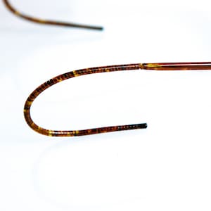 May include: A close-up of a brown and gold medical guidewire. The guidewire is flexible and has a smooth, polished finish.