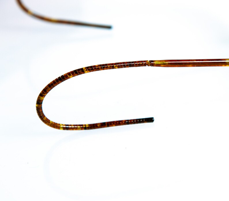 May include: A close-up of a brown and gold medical guidewire. The guidewire is flexible and has a smooth, polished finish.