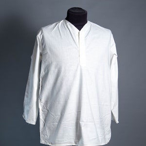 May include: A white long-sleeve shirt with a mandarin collar and a buttoned placket. The shirt is displayed on a black mannequin head against a gray background. The shirt has a relaxed fit and appears to be made of a lightweight fabric.