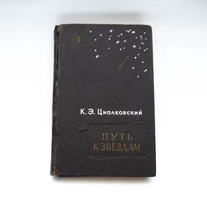 May include: A vintage book with a black cover featuring white stars and the text "K.E. Tsiolkovsky" and "Puth K Zvezdam" in gold lettering. The book has a worn appearance.