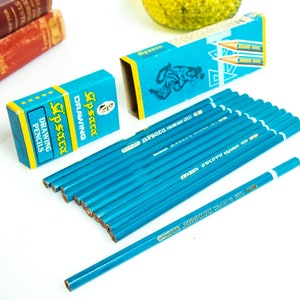 May include: A collection of blue drawing pencils with white tips and the text "Apsara Drawing 601". Two blue boxes with the text "Lipsara Drawing Pencils" are also present. The pencils are arranged on a white surface.