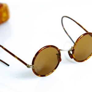 May include: Round tortoiseshell sunglasses with brown lenses and thin metal arms.
