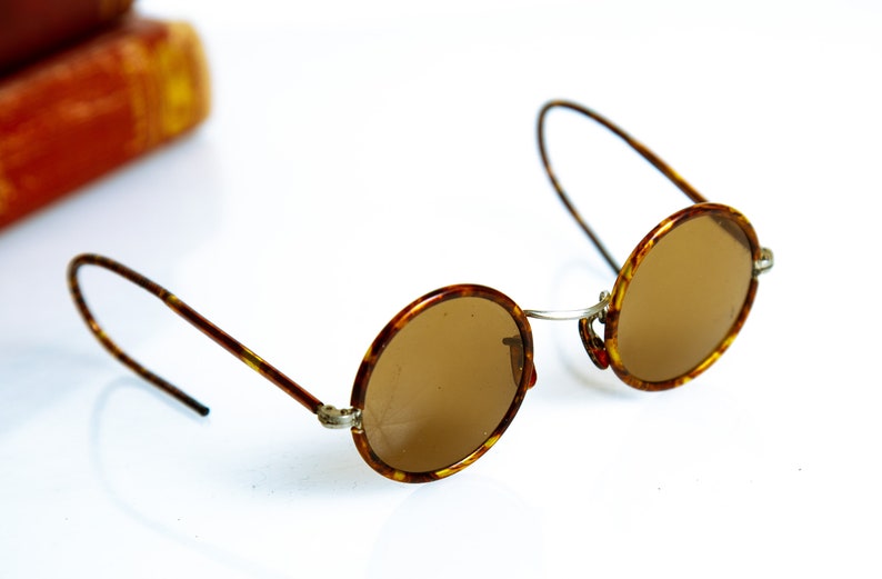 May include: Round tortoiseshell sunglasses with brown lenses and thin metal arms.