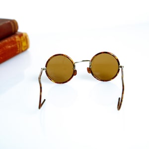 May include: Round tortoiseshell sunglasses with brown lenses and thin metal arms.