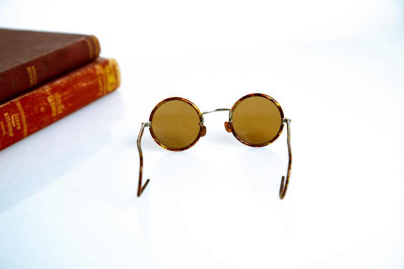 May include: Round tortoiseshell sunglasses with brown lenses and thin metal arms.
