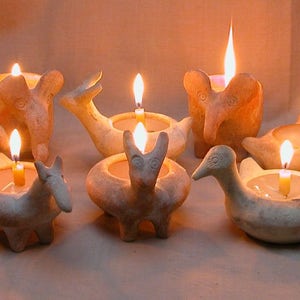 Puede incluir: Una colecci&oacute;n de portavelas de cer&aacute;mica con forma de animales, incluyendo un elefante, un p&aacute;jaro, un ciervo y un burro. Cada portavelas tiene una peque&ntilde;a vela dentro, y las velas est&aacute;n encendidas, proyectando un c&aacute;lido resplandor.