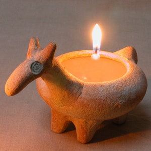 Puede incluir: Un portavelas de terracota con forma de llama con una vela encendida en su interior. El portavelas tiene un esmalte marr&oacute;n y una superficie texturizada.