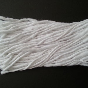 May include: A close-up of a white cotton mop head. The mop head is made of long, thin strands of cotton that are tightly packed together.