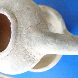 May include: A white ceramic oil lamp with a round body and a spout. The lamp has a large opening at the top for pouring oil.