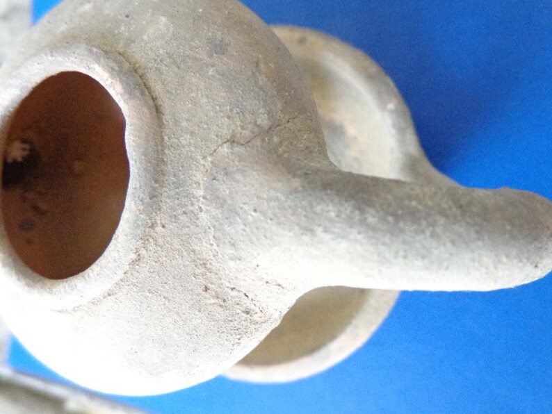 May include: A white ceramic oil lamp with a round body and a spout. The lamp has a large opening at the top for pouring oil.