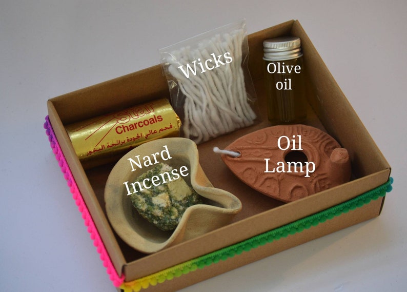 May include: A brown cardboard box with a colorful trim contains a set of items for burning incense. The box includes a small clay oil lamp, a small bowl of Nard incense, a package of wicks, a small bottle of olive oil, and a package of charcoals. The box is labeled "Charcoals" in Arabic.