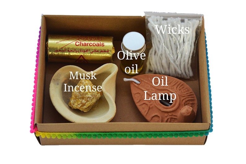 May include: A brown cardboard box with a colorful trim contains a set of items for burning incense. The set includes a small oil lamp, a bottle of olive oil, a pack of wicks, a block of musk incense, and a pack of charcoals. The box is labeled "Charcoals".