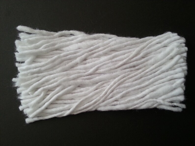 May include: A close-up of a white cotton mop head. The mop head is made of long, thin strands of cotton that are tightly packed together.
