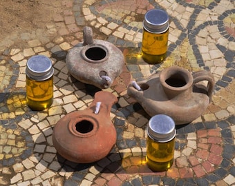 May include: Four small, brown clay oil lamps with wicks and four small glass bottles filled with a yellow liquid, all arranged on a mosaic tile floor.