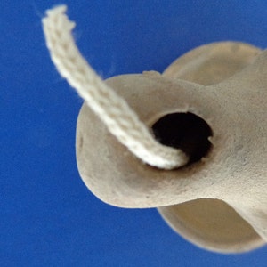 May include: A close-up of a terracotta oil lamp with a white wick. The lamp has a round body and a small opening for the wick.