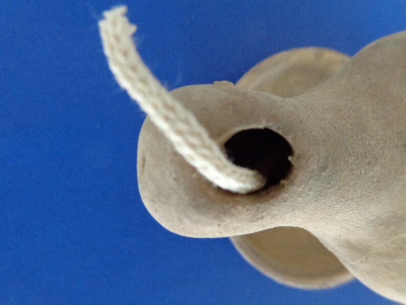 May include: A close-up of a terracotta oil lamp with a white wick. The lamp has a round body and a small opening for the wick.