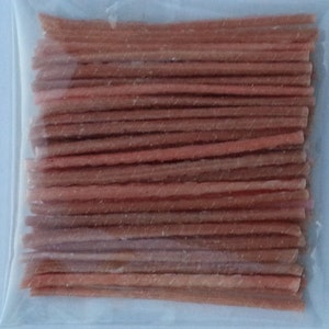 May include: A close-up of a bag of thin, pink and brown, twisted, edible sticks.