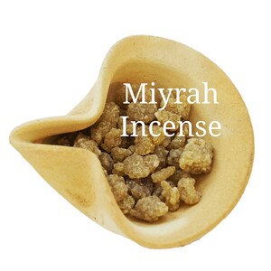 May include: A close-up of a small ceramic bowl filled with brown myrrh incense. The bowl is light brown and has a slightly textured surface. The text "Myrrh Incense" is written in white letters on the bowl.