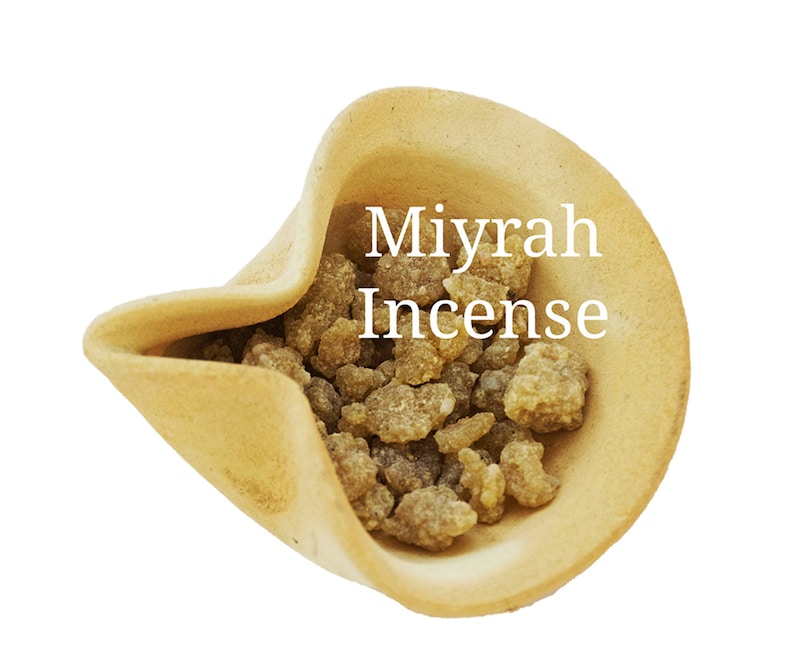 May include: A close-up of a small ceramic bowl filled with brown myrrh incense. The bowl is light brown and has a slightly textured surface. The text "Myrrh Incense" is written in white letters on the bowl.