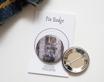Op de afbeelding: Een ronde pin met een zwart-witfoto van een standbeeld voor een gebouw. De tekst "GLASGOW" is in wit op de pin gedrukt. De achterkant van de pin is zilverkleurig met een pin en een veiligheidssluiting. De pin ligt op een witte achtergrond met een kaart waarop "Pin Badge" en "Sofia Alves Photographie" staat.