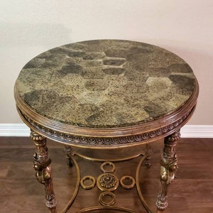 May include: A round side table with a patterned, mottled green and brown top. The table has ornate gold-colored legs and a decorative apron. The table is approximately 24 inches in diameter and 28 inches tall.