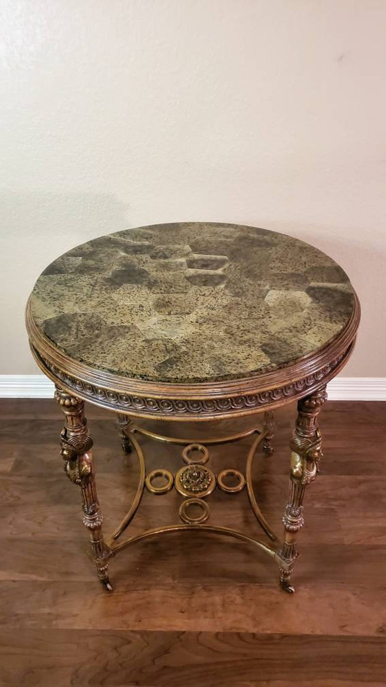 May include: A round side table with a patterned, mottled green and brown top. The table has ornate gold-colored legs and a decorative apron. The table is approximately 24 inches in diameter and 28 inches tall.