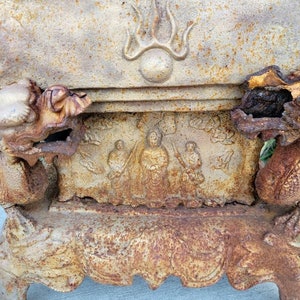 May include: A vintage cast iron incense burner with a dragon design. The burner has a rectangular base with four legs and a raised top with a dragon head on each side. The top of the burner has a relief design of a Buddha figure surrounded by two figures. The burner is rusty and shows signs of wear.