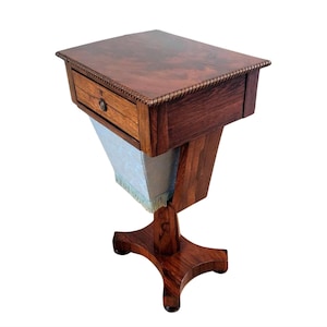 May include: A dark wood side table with a single drawer and a turned pedestal base. The table has a decorative trim around the top edge.