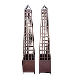May include: Two tall, brown metal obelisks with a lattice design. Each obelisk has a square base and a triangular top. The open lattice structure allows for climbing plants, making them suitable for a garden or outdoor space.
