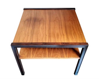Puede incluir: Una mesa auxiliar cuadrada de madera con marco marrón oscuro y dos estantes. Los estantes superior e inferior son de color marrón claro, mientras que el marco es marrón oscuro. La mesa mide aproximadamente 61 cm de ancho y 61 cm de largo.