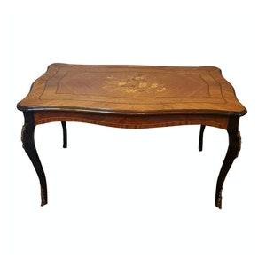 May include: A rectangular wooden table with a marquetry top featuring a floral design. The table has four legs with a curved design and black painted accents.