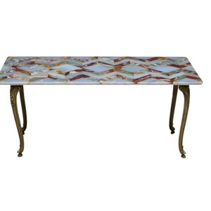 May include: A rectangular coffee table with a geometric pattern of inlaid marble in shades of blue, green, red, and white. The table has four ornate brass legs.