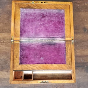 May include: A wooden writing desk with a hinged lid and a purple velvet interior. The desk has a small compartment with dividers and a long drawer.